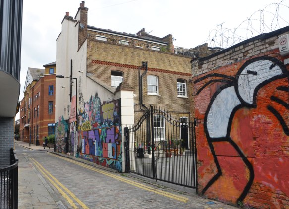 looking up a street, Chilton St., two buildings and a fence with a lot of street art on them. 