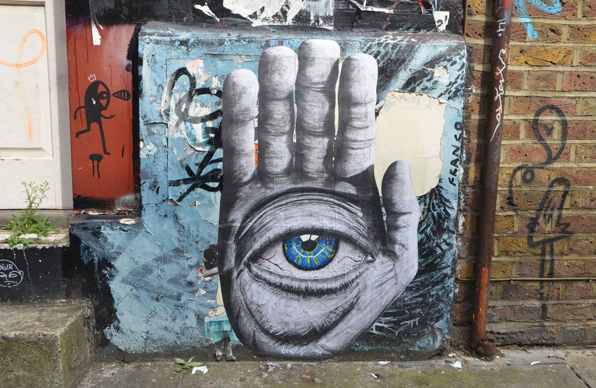 street art, paste up of a very large hand, palm facing frontwards with a large very realistic looking blue eye in the center of the palm. 