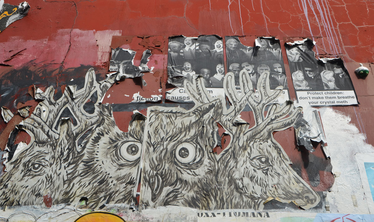 a paste up of an owl and two deers that is starting to peel, it partially covers three poster pasteups that are even more frayed. 