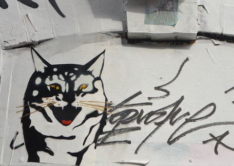 black outline drawing stencil of a cat's head, with added yellow eyes and red tongue 