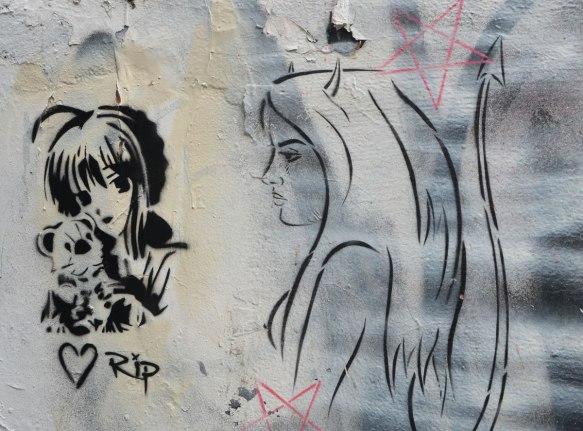 stencil of woman with pet, drawn like a Japanese anime girl, beside her is a line drawing, in black of a woman's head and shoulders in profile, 2 red pentaon shaped stars 