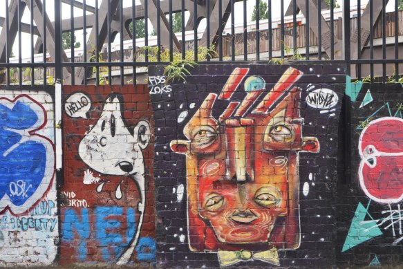 a street art painting of a head abstracted, squarish, with 4 eyes by widyz and another little white character saying hello beside it. 