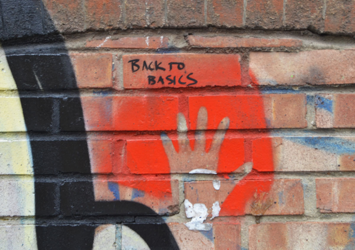 graffiti made of a handprint, hand on brick wall, spray with red, leave make of handprint. SOmeone has written, back to basics above the hand