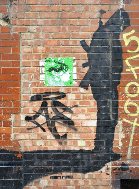 street art in black of a silhouette of a soldier with weapon on back, looking down at the precipice that he's standing on as it starts to crumble