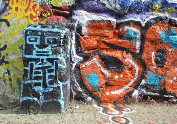 short black pillar between street and building has been painted black and then blue line drawing of a square headed man with arms and ribs. 