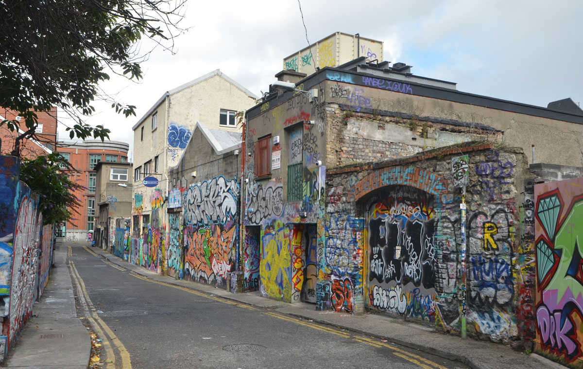 a narrow street with low buildings on both sides, walls of which are covered with graffiti 