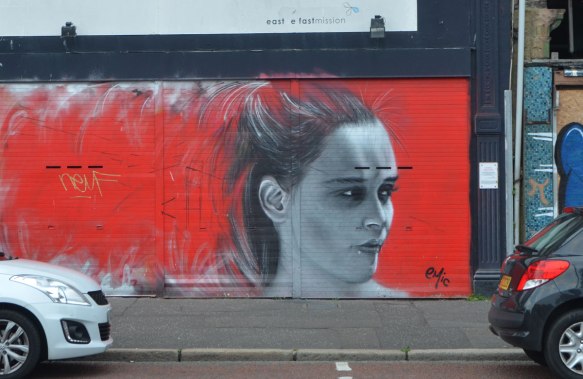 mural by emic, head and face of a young woman looking to the right, in grey tones (black and white) on a bright red background. 