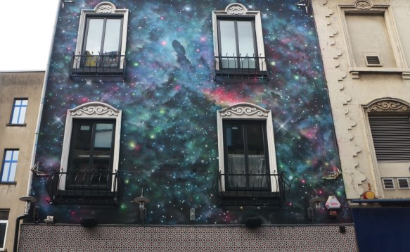 The front of a house, upper storeys, covered with a painting that looks a bit like an imaginative version of the stars at night. The universe and beyond. 