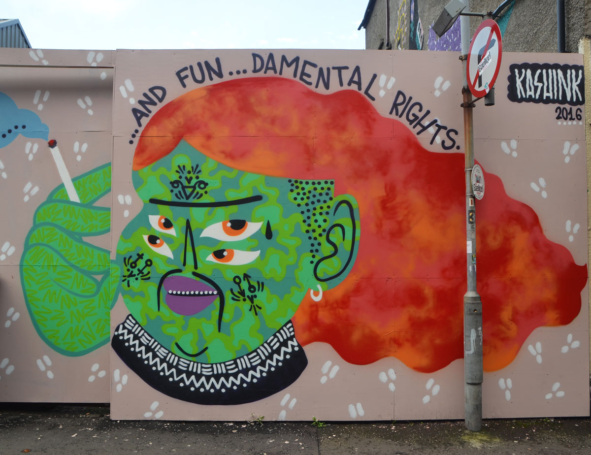 mural by Kashink of person with green face, four eyes and long bushy reddish orange hair. Words say and fun--damental rights. Person is smoking (green hands)