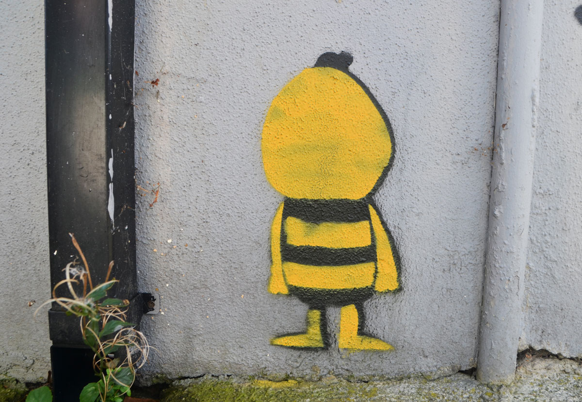little street art painting of a yellow and black little guy with face towards the wall (or is faceless)