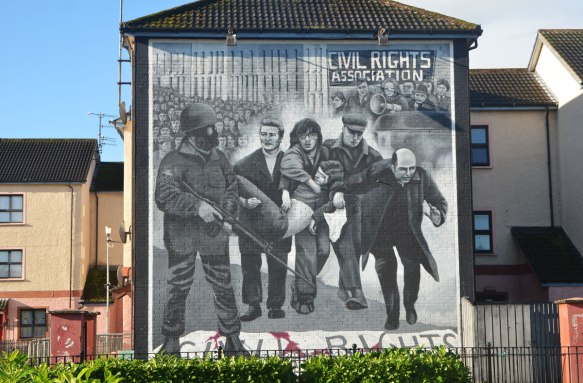 Free Derry mural in Bogside, Derry Northern Ireland, in shades of grey, commemorating Bloody Sunday in 1972 - a priest with his head down carries a white flag as people carry an injured man 