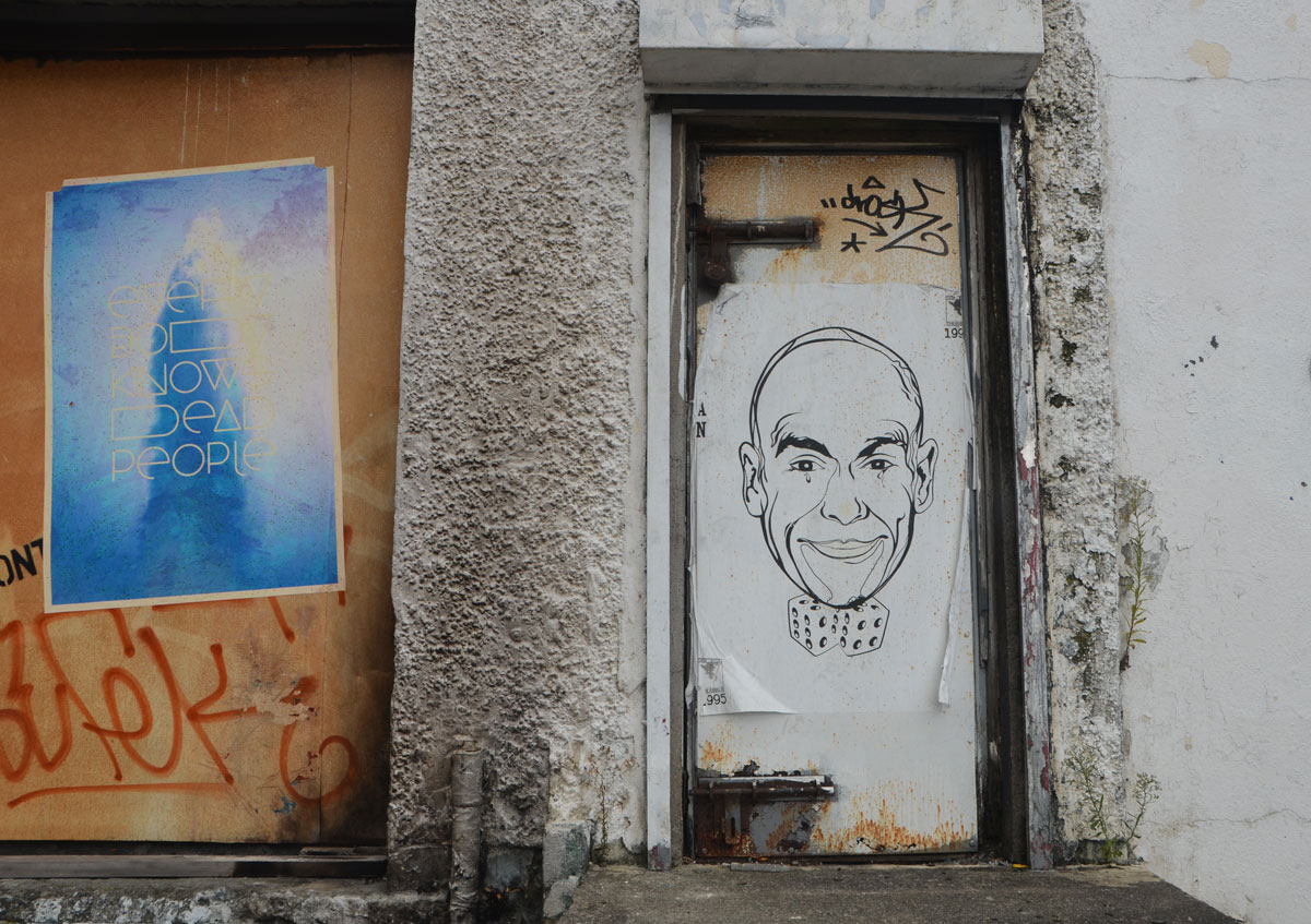 large paste up of a man's head on a door of a grubby dirty white wall.