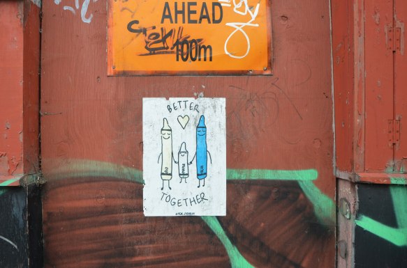 a poster of three crayons standing together and holding hands. The one in the middle is purple and it's shorter, On either side is red and blue. At least that's what the words say, only the blue has been coloured in, signed #peachydublin