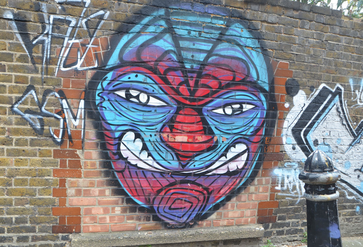 street art painting on a brick wall of a large face in red and blue with some whites in the eyes and some white teeth.