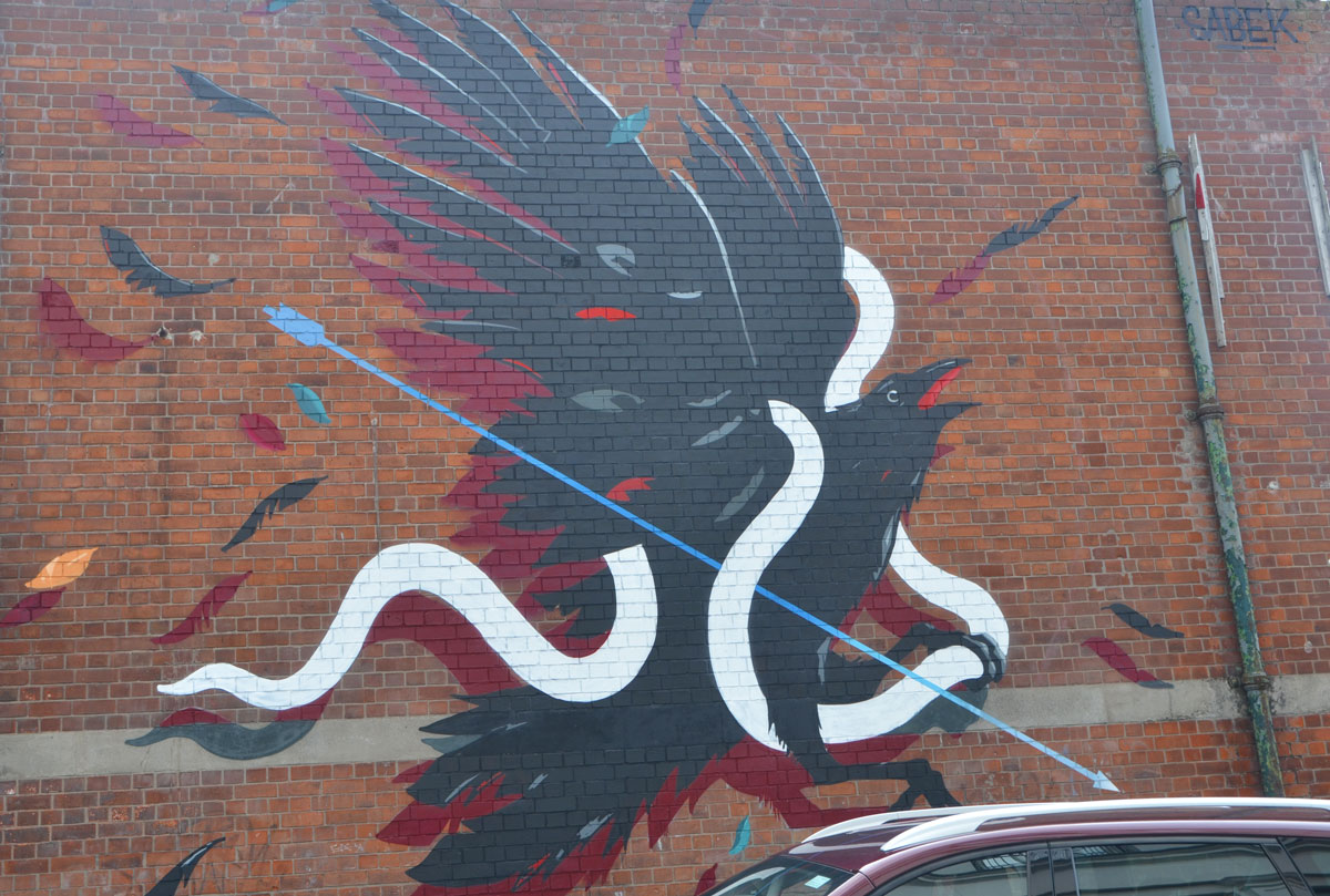 mural by sabek of a black bird caught up in a white ribbon as it tries to fly