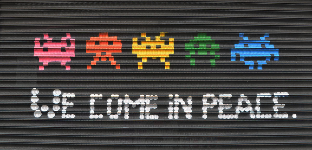 a line of 5 space invader creatures from the video game, with the words we come in peace under them.
