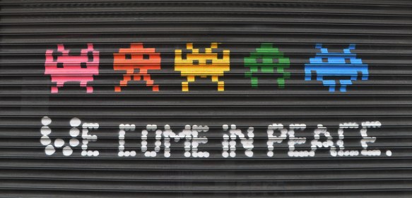 a line of 5 space invader creatures from the video game, with the words we come in peace under them. 