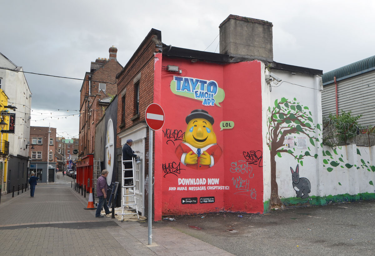 an ad for Tayto emoji app, red mural with yellow faced man cartoonish character 