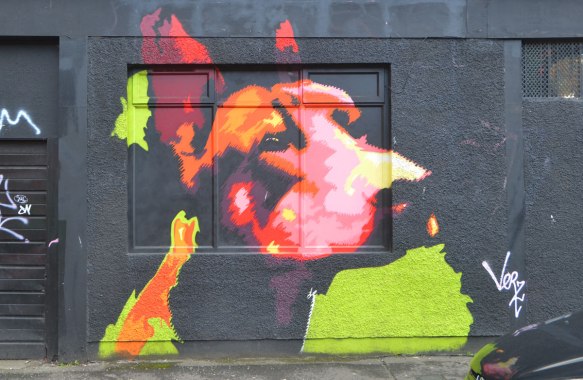 mural on black wall of a dog's head and neck in oranges, red, and pinks, 