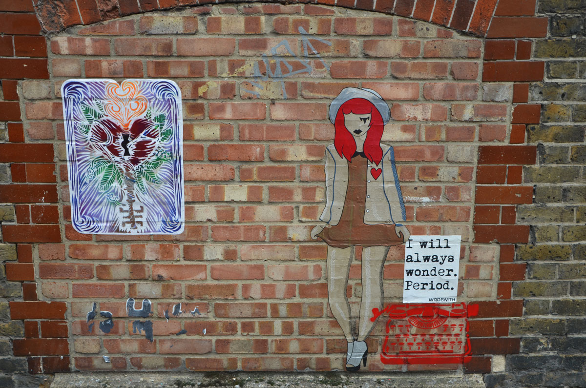 three pieces of street art, a poster with drawing of flower in pink and red with blue background, a red wordsmith typewriter with a page that says I will always wonder. period. and lastly, a girl, standing, almost life sized, with red hair and a red heart on her cardigan.