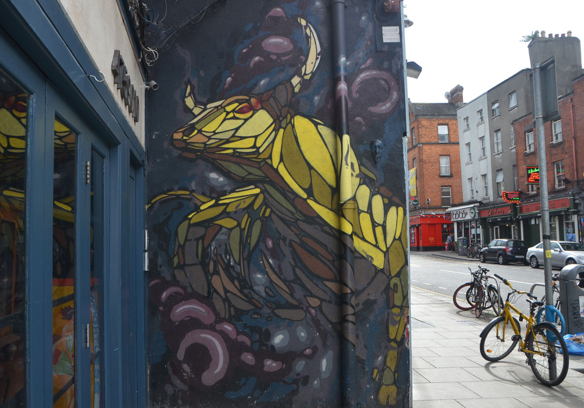 mural of a yellow horned animal on the side of a store, beside the sidewalk