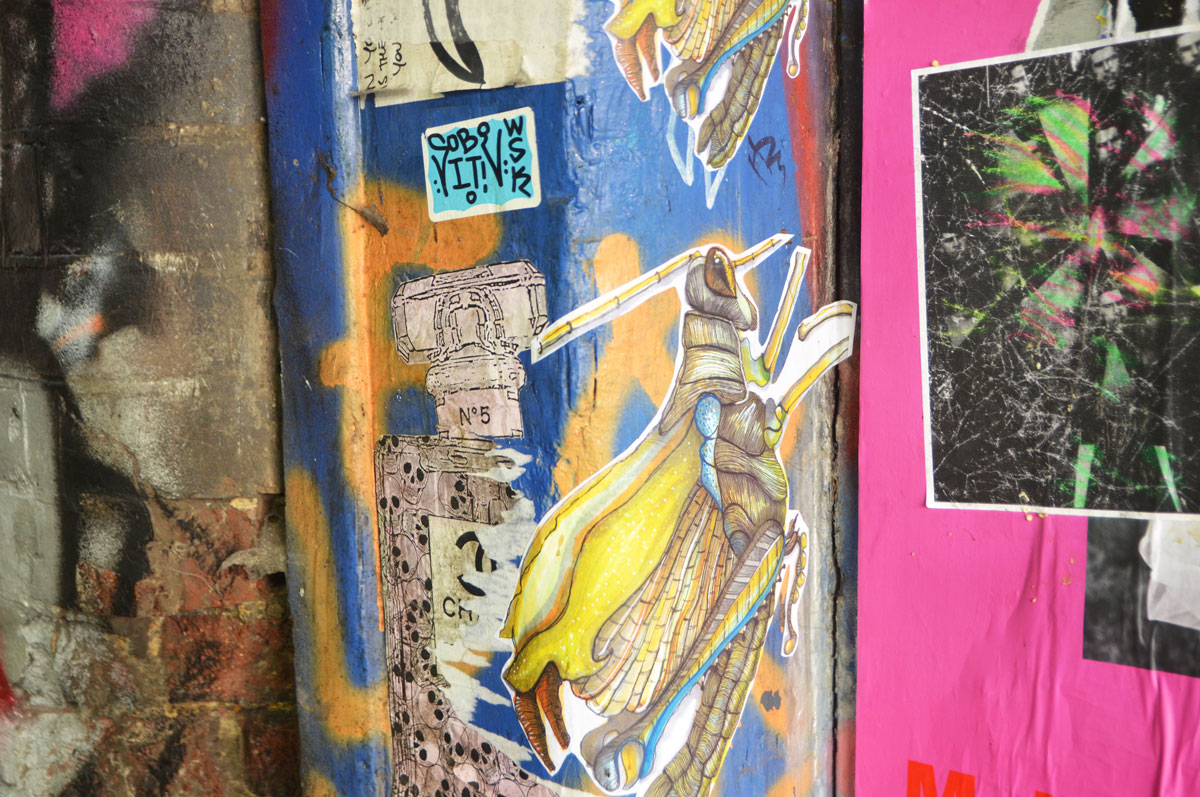 street art and graffiti in Shoreditch England, on Braithwaite Street, a grasshopper paste up, an old chanel number 5 perfume bottle 