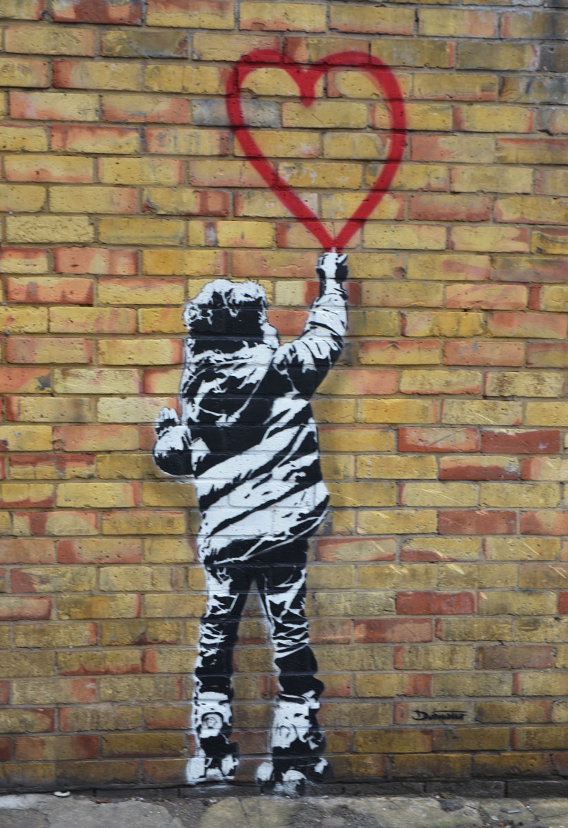 child in winter jacket, drawn in black and white on a brick wall, reaching up and touching the bottom point of a red heart. 
