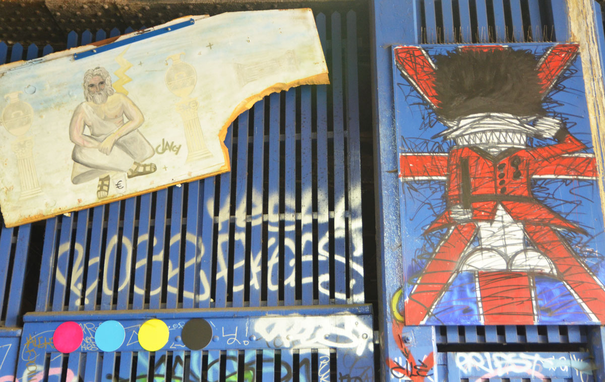 street art and graffiti in Shoreditch England, on Braithwaite Street, a painting of a Buckingham palace guard with its bushy black hat and red uniform, on a union jack by Nathan Bowen and a drawing of a man sitting on a sidewalk by Clancy 