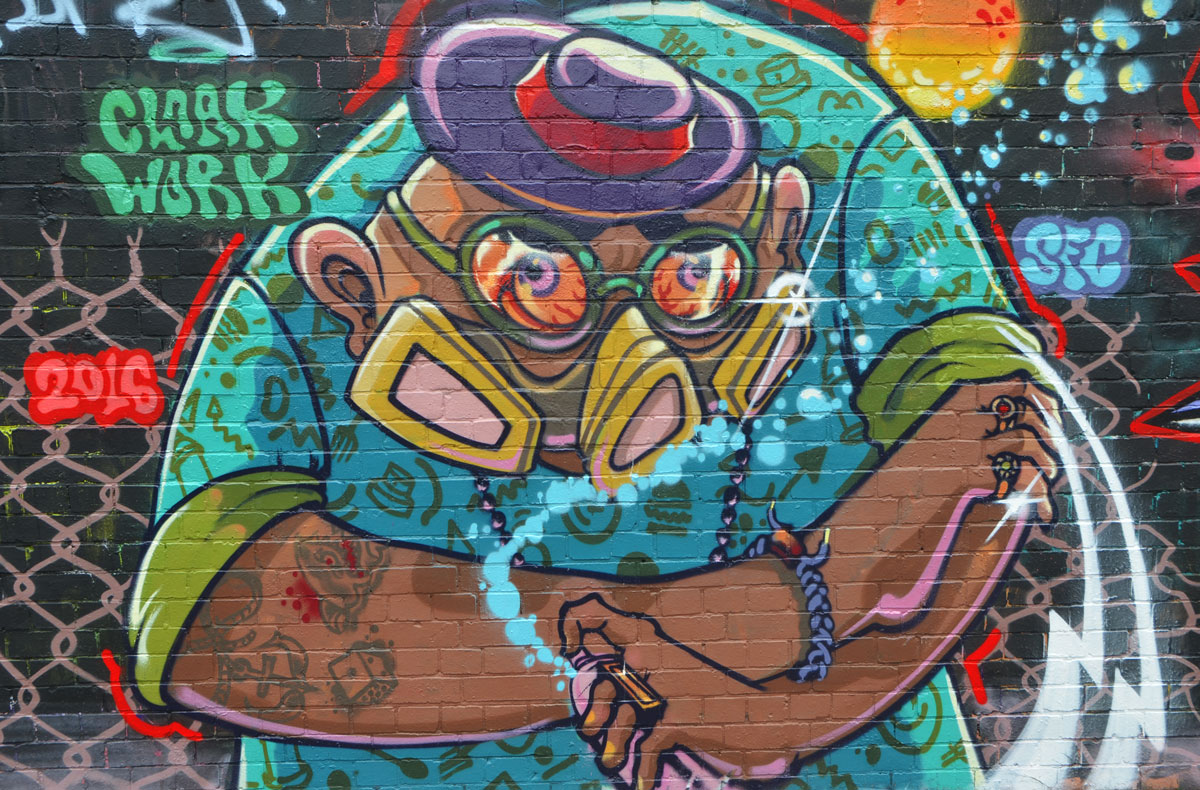 street art and graffiti in Shoreditch England, on Braithwaite Street, mural of a large fat man with gas mask on and spray paint can in hand by cloak work 
