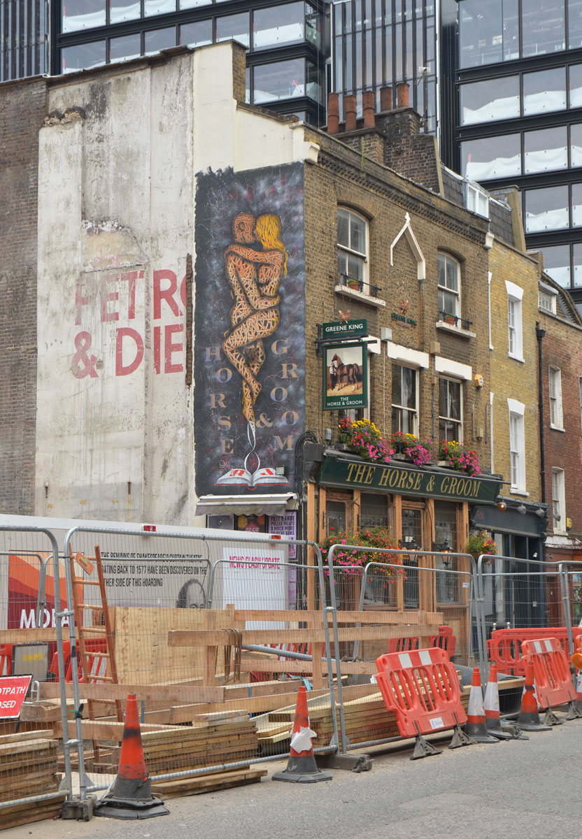 road construction, some older brick buildings and new skyrises in the background. On the wall of the Horse and Groom is a large vertical mural of a naked couple embracing while standing up