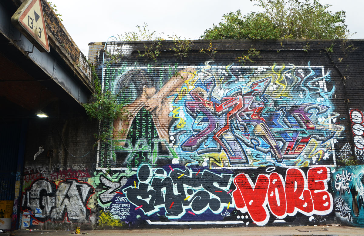 street art and graffiti in Shoreditch England, on Braithwaite Street, large mural of a woman with back to viewer, lifting up the skin on her back to reveal digital codes