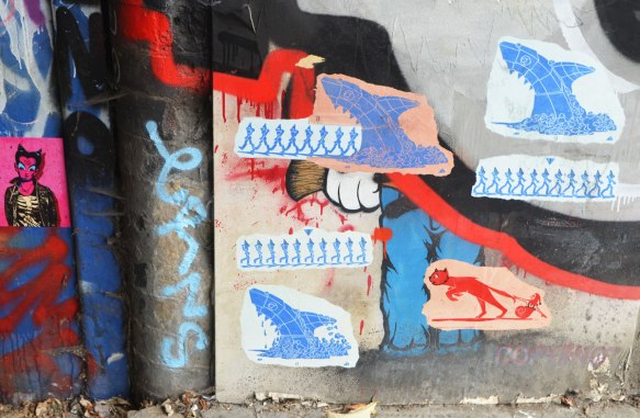 street art and graffiti in Shoreditch England, on Braithwaite Street, six or seven paste ups on a wall, including a Lt. Vincent being pulled by a cat 