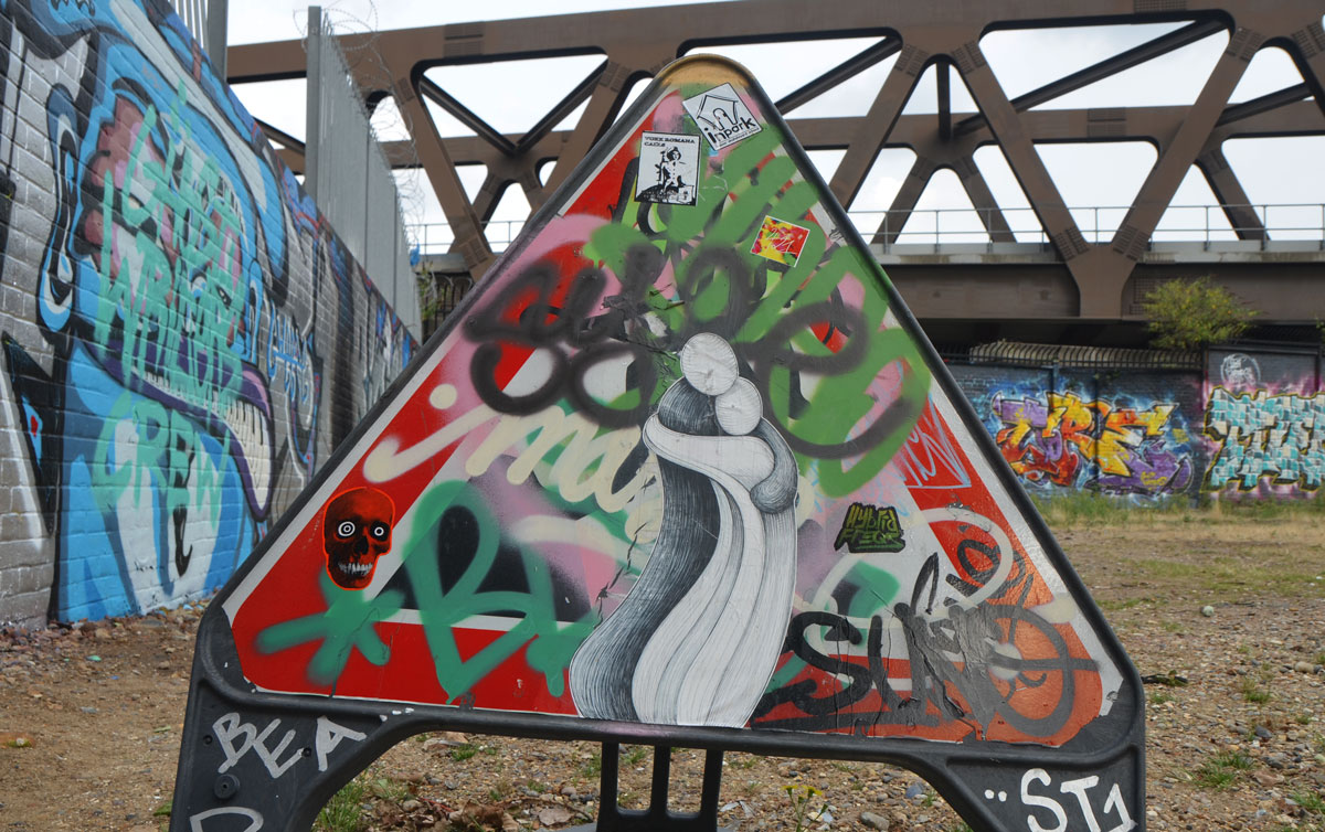 triangular street sign with red border, unreadable because covered with stickers and spray paint 