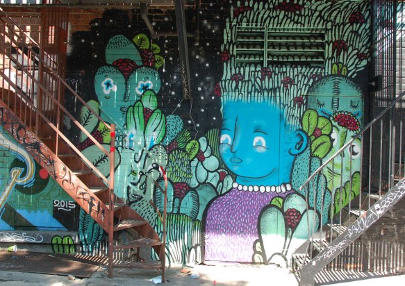 under a balcony with two sets of stairs in front of it, a mural with a blue faced girl as well as some other creatures 