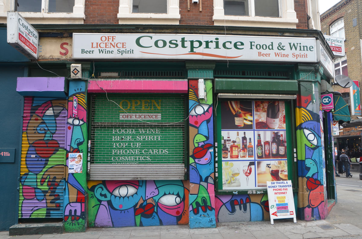 a photo of a costprice store, an off licence beer, wine and spirits merchant, as well as food. A painting of multicoloured colourfuil abstract faces covers all surfaces. 