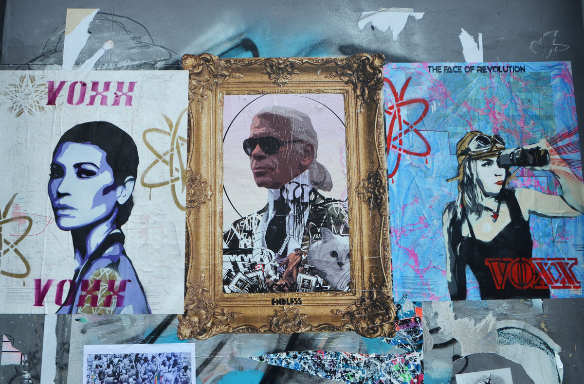 three pasteups on a wall, poster size, two by voxx and one in the middle by endless. Karl Lagerfeld is the subject in the endless paste up - with dark sunglasses and a wild patterned jacket, a fancy gold frame is around him, 