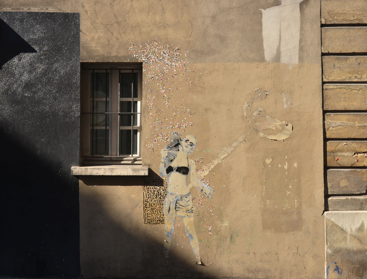 large size paper paste up of a young woman, standing, with a lot of small glittery pieces of paper scattered around her - wearing a black bra top and shorts