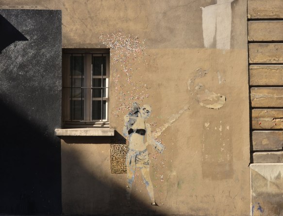 large size paper paste up of a young woman, standing, with a lot of small glittery pieces of paper scattered around her - wearing a black bra top and shorts