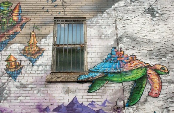street art, graffiti, animals painted on a wall - a turtle flying in the clouds past a real window, with small buildings on its back