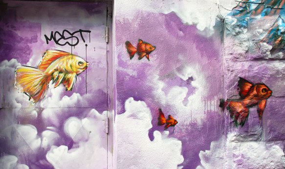 street art, graffiti, animals painted on a wall - yellow and orange fish swimming in a purple sky with puffy clouds