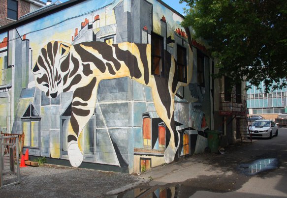 mural of a large tabby cat lying on rooftops with its paw hanging over the side of the buildings