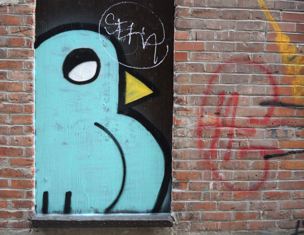 street art, graffiti, animals painted on a wall - a large stylized pale blue bird in a window of a red brick building.