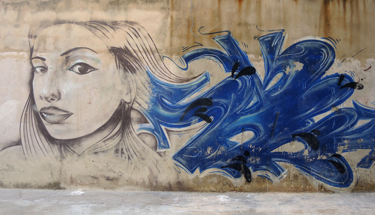 a street art picture of a young woman's head and face, she is looking slightly back over her shoulder. Blue abstract beside her