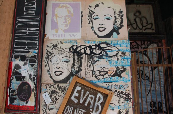 5 poster of Marilyn Monroe on a wall. The 6th poster has been covered by a poster of a man, Bill W. 