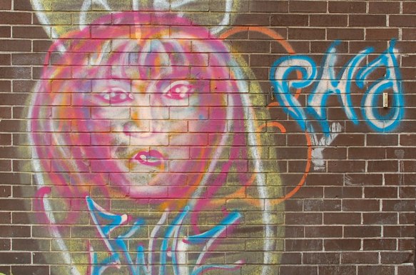 painted face on a brick wall, pink and yellow