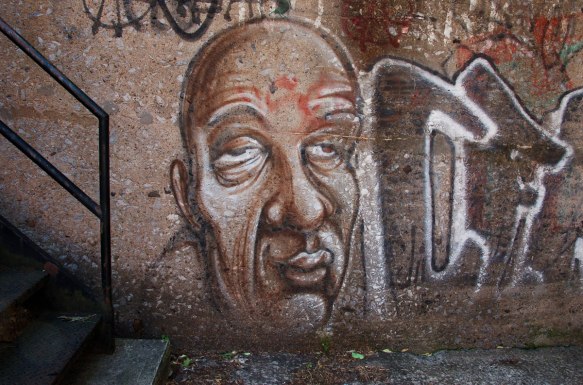 brown street art painting of a blad man's head and face with droopy eyes partially closed and wrinkled foreheard and cheeks 