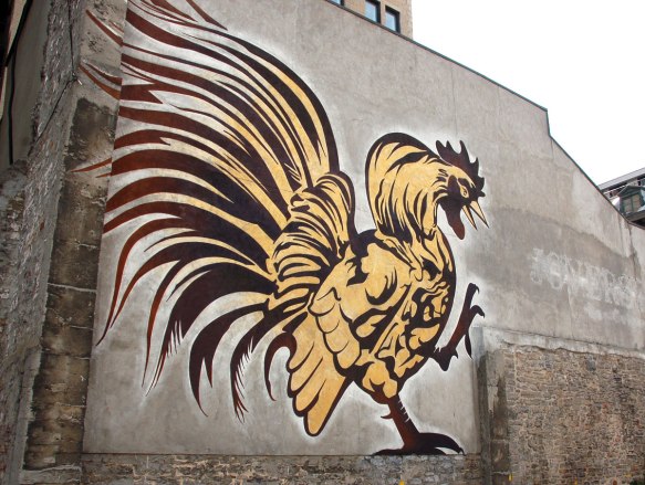 mural painting of a very large yellow and brown rooster on the side of two storey building in downtown Montreal