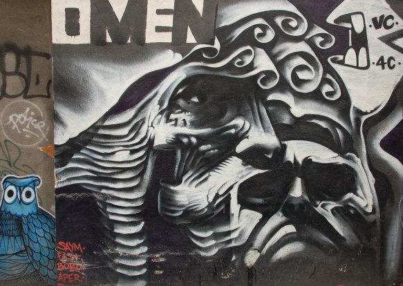 a multifaceted face in grey tones by omen, with a small pasteup (or painting?) of a blue owl beside the face 