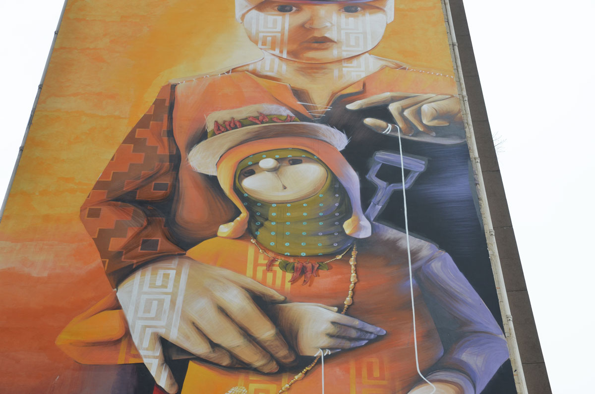 part of a large multi storey vertical mural on the side of an apartment building in Paris called 'Our Utopia is Their Future' by inti - a child is working a puppet who in turn has a small puppet on a string 