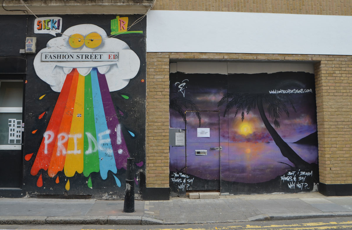 two murals. on the left, a large white cloud with yellow eyes and three white upper teeth is spitting out a rainbow that someone has written pride on the top of . The other mural is a sunset scene with a palm tree and beach in silhouette in the foreground, purple sky and water, yelloish orange sun and reflections in the water. 